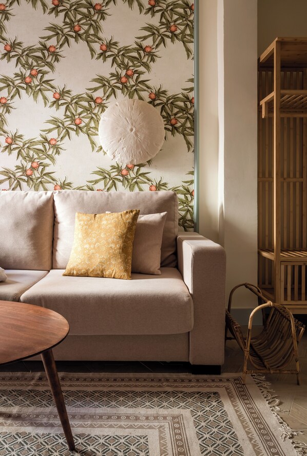 Un salon chaleureux avec un canapé, un coussin décoratif à motifs, une table ronde et une chaise en osier.