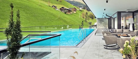 Zona de piscina con vistas a una colina, mobiliario exterior y barandilla de vidrio.