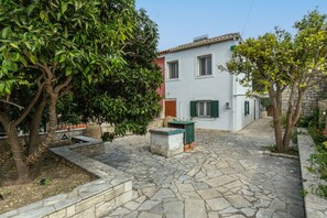 A courtyard with stone flooring, a white building with green shutters, and a tree with dense foliage. - Country House 'Serenity' with Private Terrace, Wi-Fi, and Air Conditioning (Paxoi)
