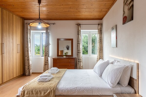 A bedroom with a wooden ceiling, a bed with white linens, a wooden dresser, and a window with curtains.