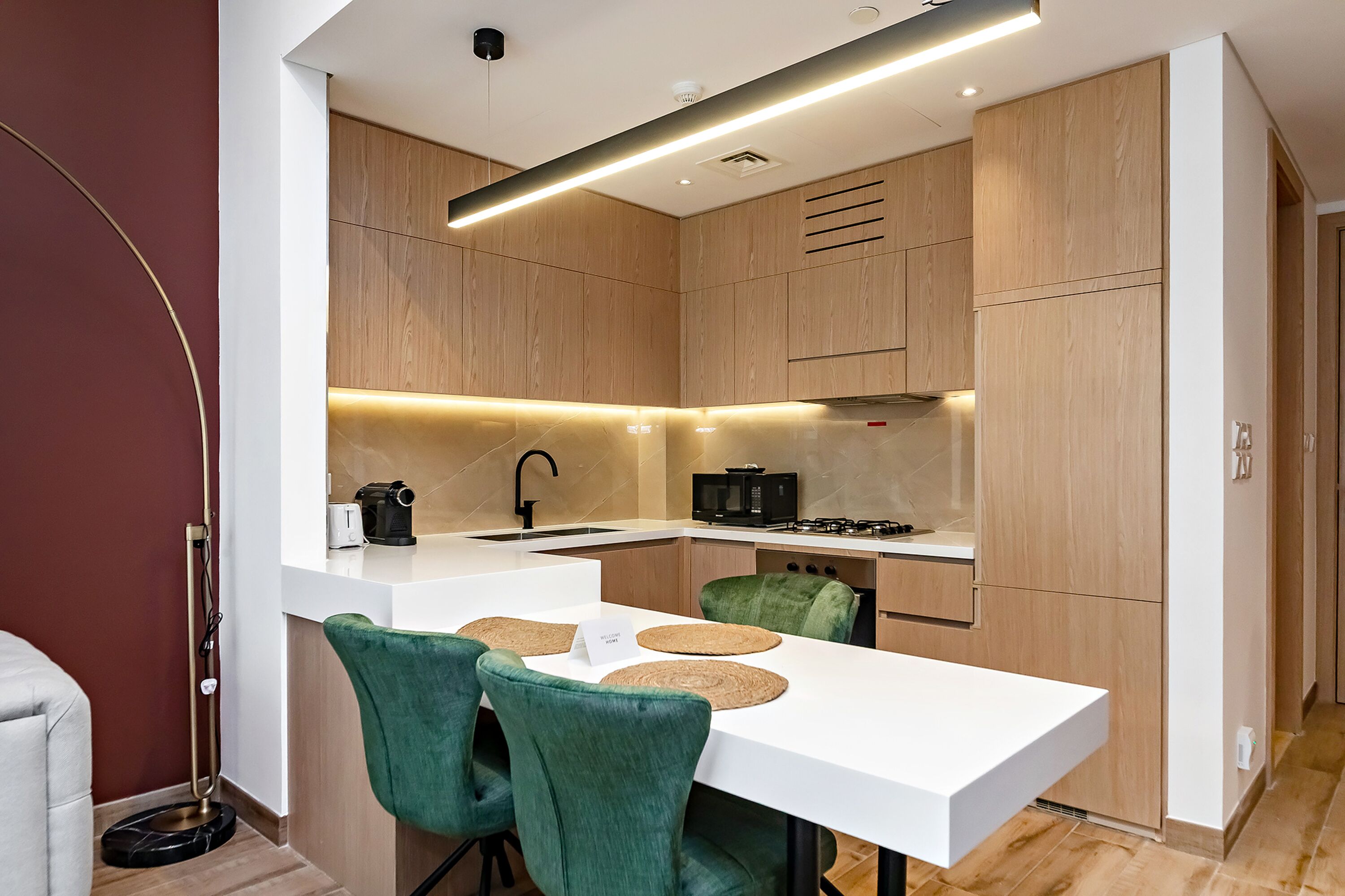 Une cuisine moderne avec des meubles en bois, un plan de travail blanc et un coin repas avec des chaises vertes.