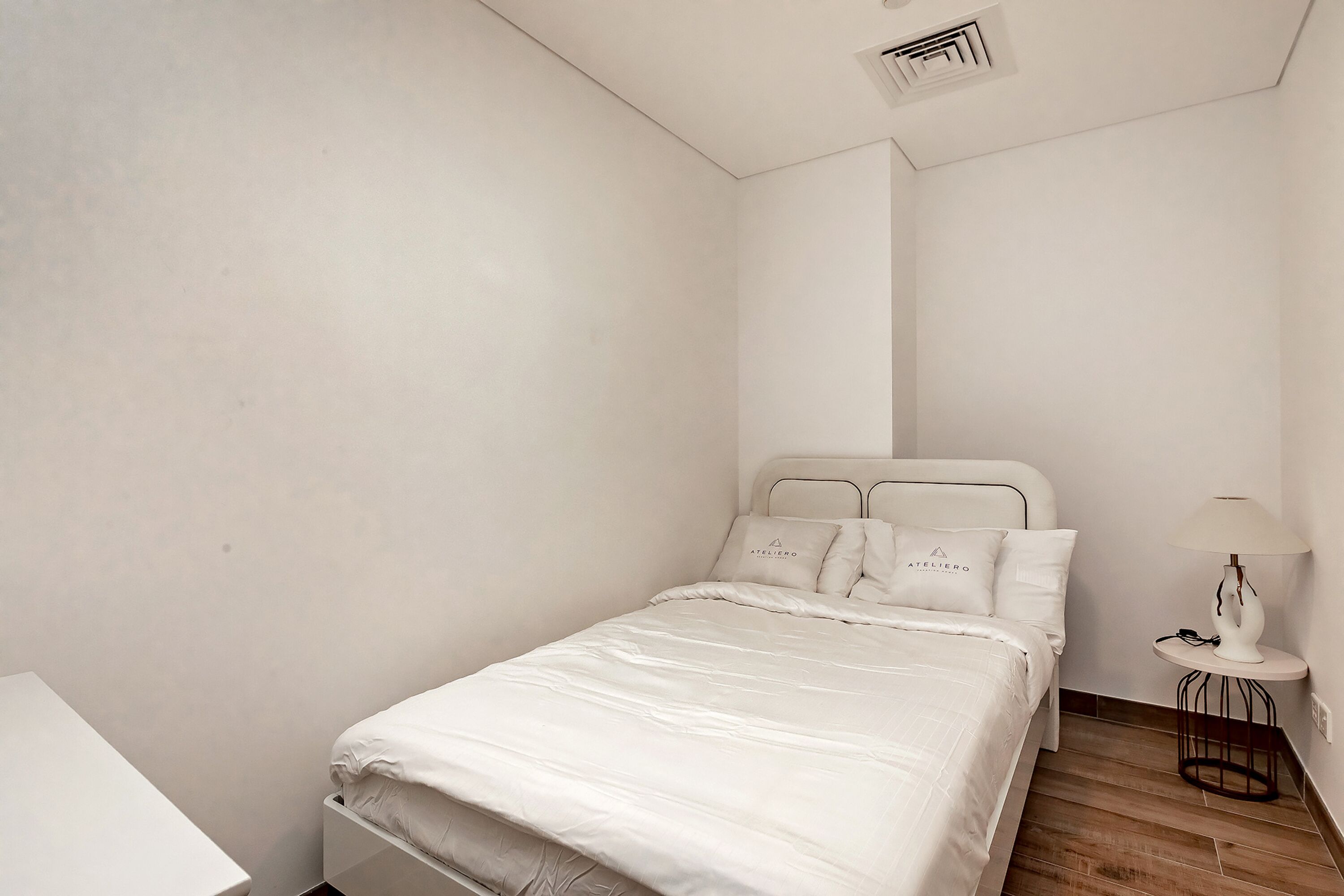 Een minimalistische slaapkamer met een bed, nachtkastje en een lamp.