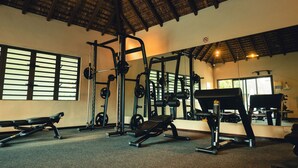 Een sportschool met diverse fitnessapparatuur, grote ramen en een hoog plafond met houten balken.