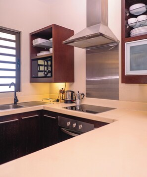 Una cocina moderna con armarios oscuros, una campana de acero inoxidable, horno empotrado y pileta doble.