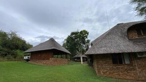 A rural setting with thatched-roof buildings, a grassy lawn, and a vehicle in the background.