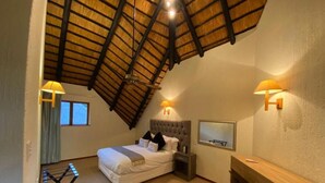 A bedroom with a sloped ceiling, a bed, bedside lamps, a desk, and a window.