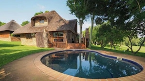 A swimming pool with a brick border, surrounded by a paved area.