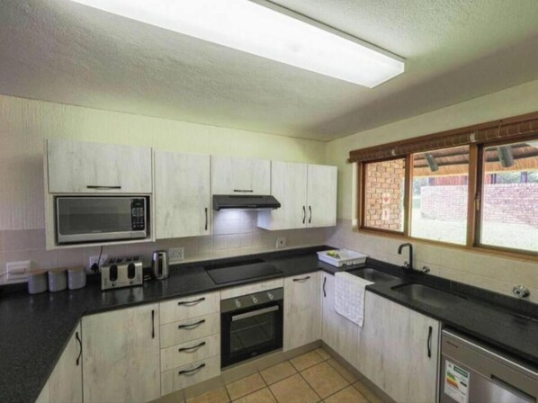 A kitchen with white cabinets, a microwave, a stove, and a sink. - Kruger Park Lodge Unit 550 (Hazyview, Kruger Park Lodge)