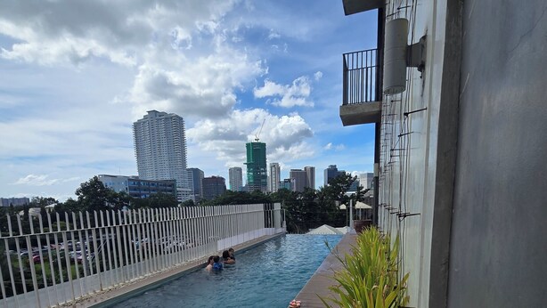 A swimming pool with a wooden deck, surrounded by a white fence, and a view of a cityscape with tall buildings in the background. - Studio Unit Condo near Ayala Center Cebu w/Netflix & Fast Wifi
(Ohana Suites#1) (Cebu City)