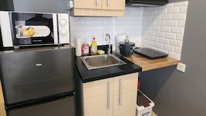 A compact kitchen with a black refrigerator, a microwave, a sink, and wooden cabinets. - Studio Unit Condo near Ayala Center Cebu w/Netflix & Fast Wifi
(Ohana Suites#1) (Cebu City)