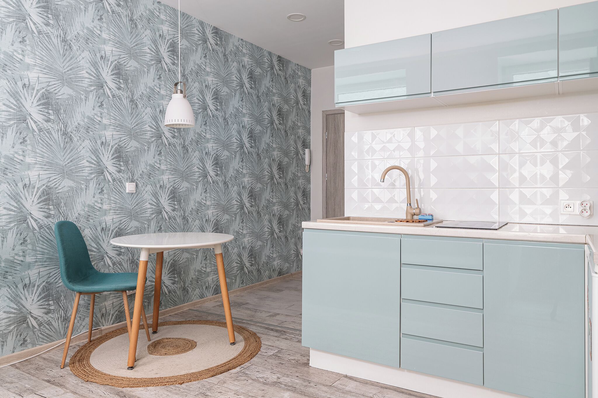 A modern kitchen with light blue cabinets, a white countertop, and a patterned backsplash.