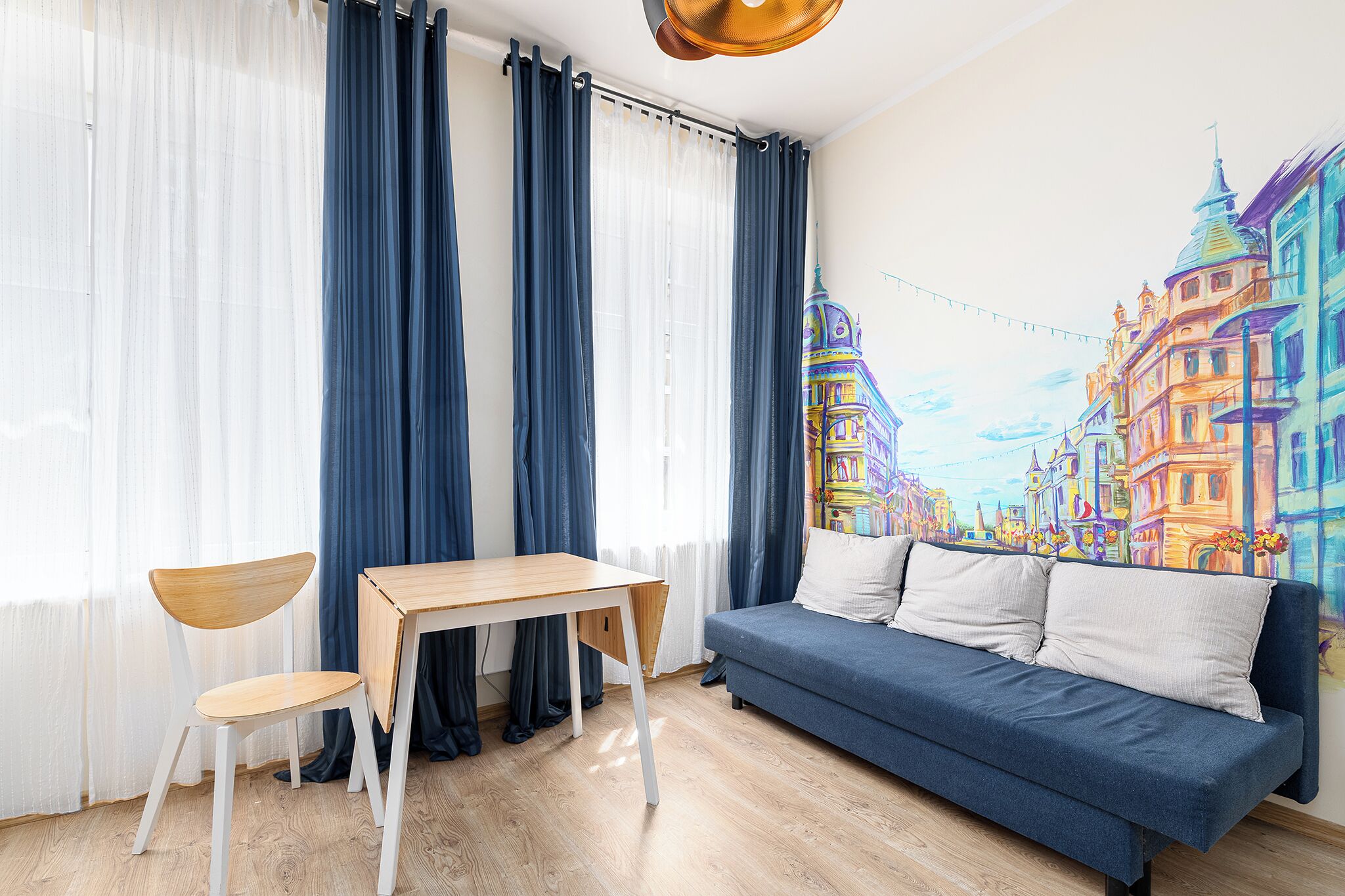 A room with a wooden desk, a blue sofa, and a colorful mural on the wall.