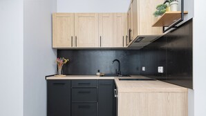 Cozinha moderna com armários de madeira clara, eletrodomésticos pretos e uma pequena planta no balcão.