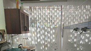 A kitchen with white tiled walls, a sink, cabinets, and a window with a curtain. - Aldeia da Mata - near the sea (Arraial d'Ajuda)