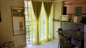 A kitchen with a dining area, a window with curtains, and a tiled backsplash. - Aldeia da Mata - near the sea (Arraial d'Ajuda)