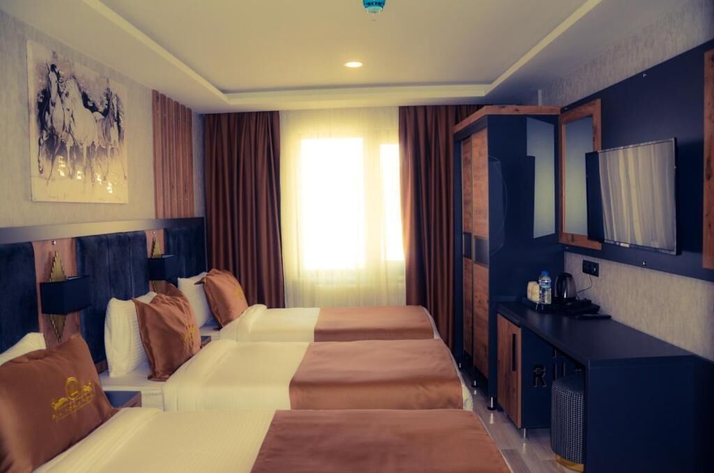 A hotel room with two beds, a desk, a mirror, and a large window with curtains.