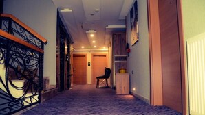 A hotel hallway with a carpeted floor, a wooden staircase with a metal railing, and a chair near the end. - RUA WORLD HOTEL (Van)