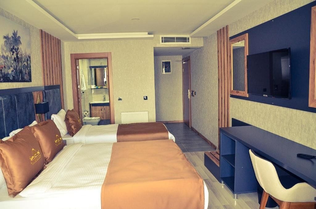 A hotel room with two beds, a desk, a TV, and a bathroom.