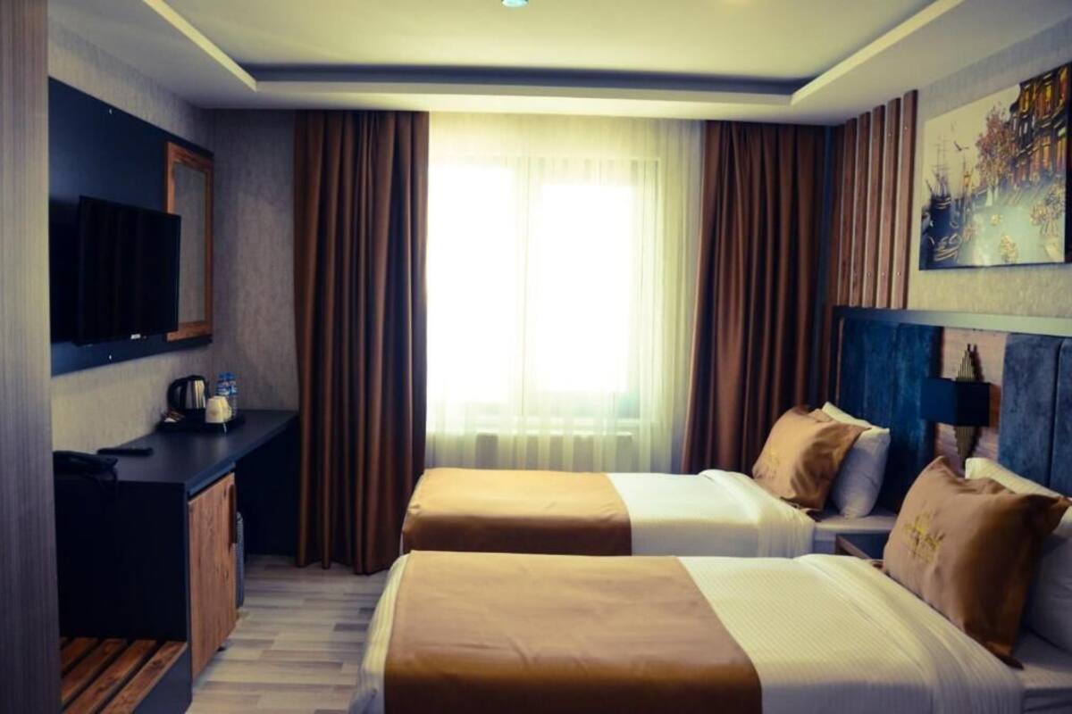 Ein Hotelzimmer mit zwei Betten, einem Schreibtisch, einem Flachbildfernseher, einer Kaffeemaschine und einem Bild an der Wand.