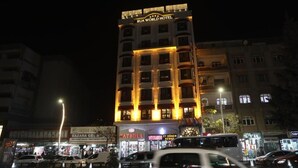 A multi-story hotel with illuminated signage, surrounded by various shops and vehicles. - RUA WORLD HOTEL (Van)