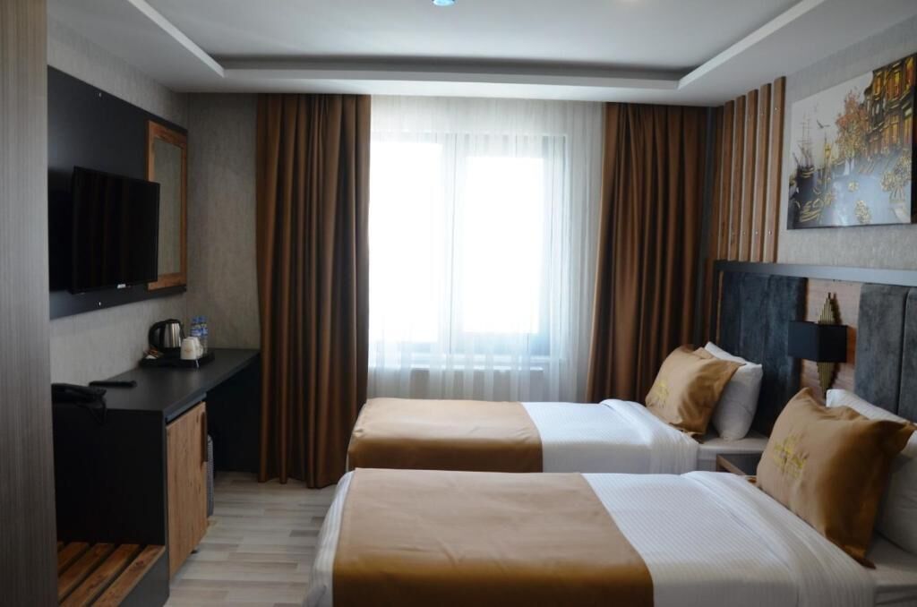 A hotel room with two beds, a desk with a television, and a large window with curtains.