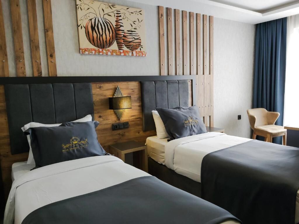 A hotel room with two beds, a wooden headboard, a wall-mounted lamp, and a decorative painting.