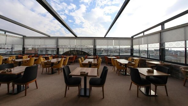 A rooftop dining area with multiple tables and chairs, large windows offering a city view. - RUA WORLD HOTEL (Van)