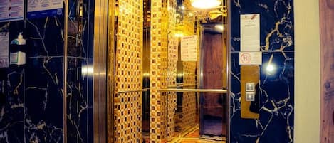 An elevator with marble walls and a patterned floor, featuring a handrail and emergency buttons.