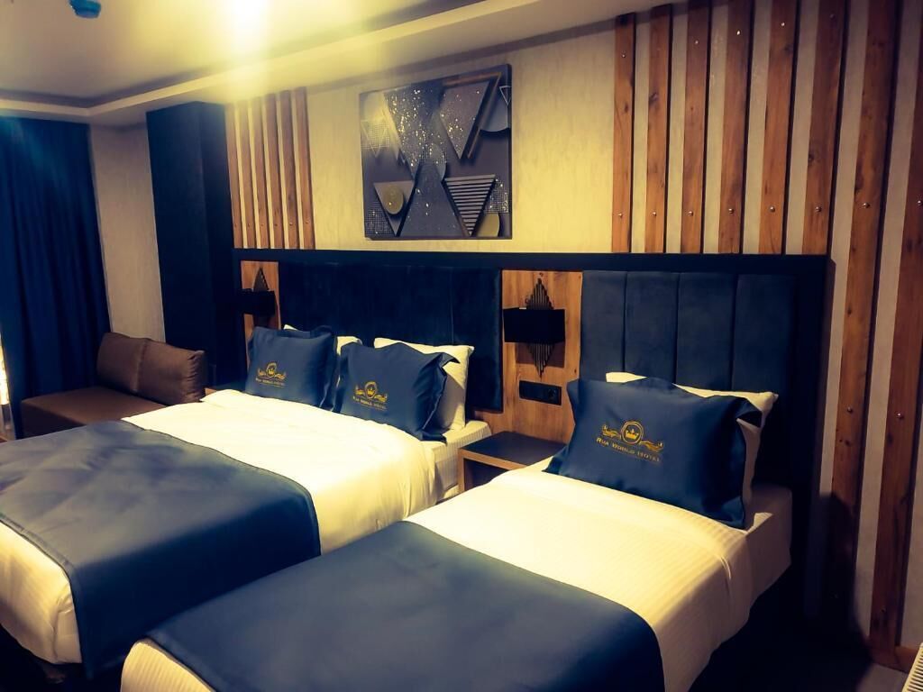 A hotel room with two beds, each with matching headboards and pillows, and a wooden panel wall.