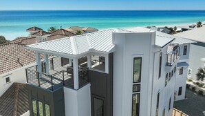 Un edificio moderno con tetto piatto e ampie finestre, affacciato su una spiaggia con acque blu cristalline.