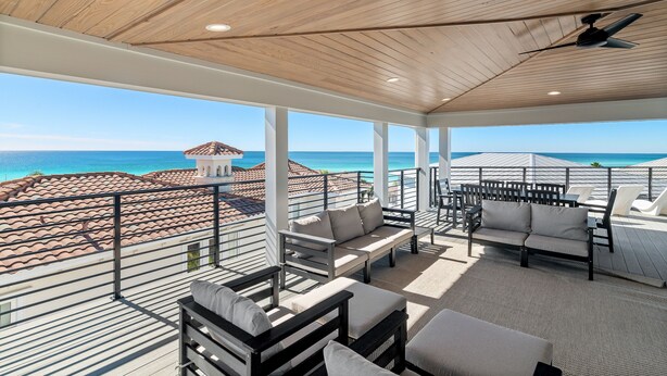 Area salotto esterna coperta con vista sull'oceano, caratterizzata da un soffitto in legno, pilastri bianchi e diverse tipologie di posti a sedere.