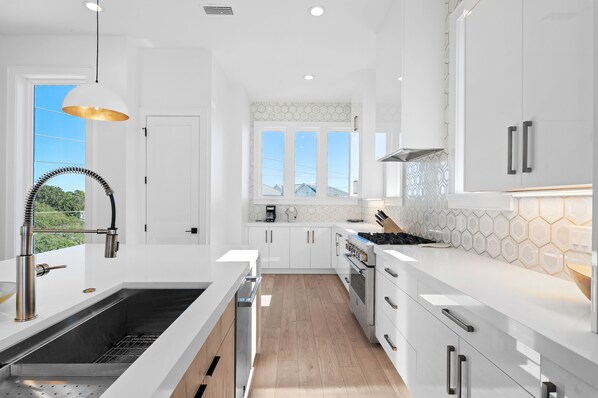 Cocina moderna con muebles blancos, pileta de acero inoxidable y ventana con vista a un paisaje verde.