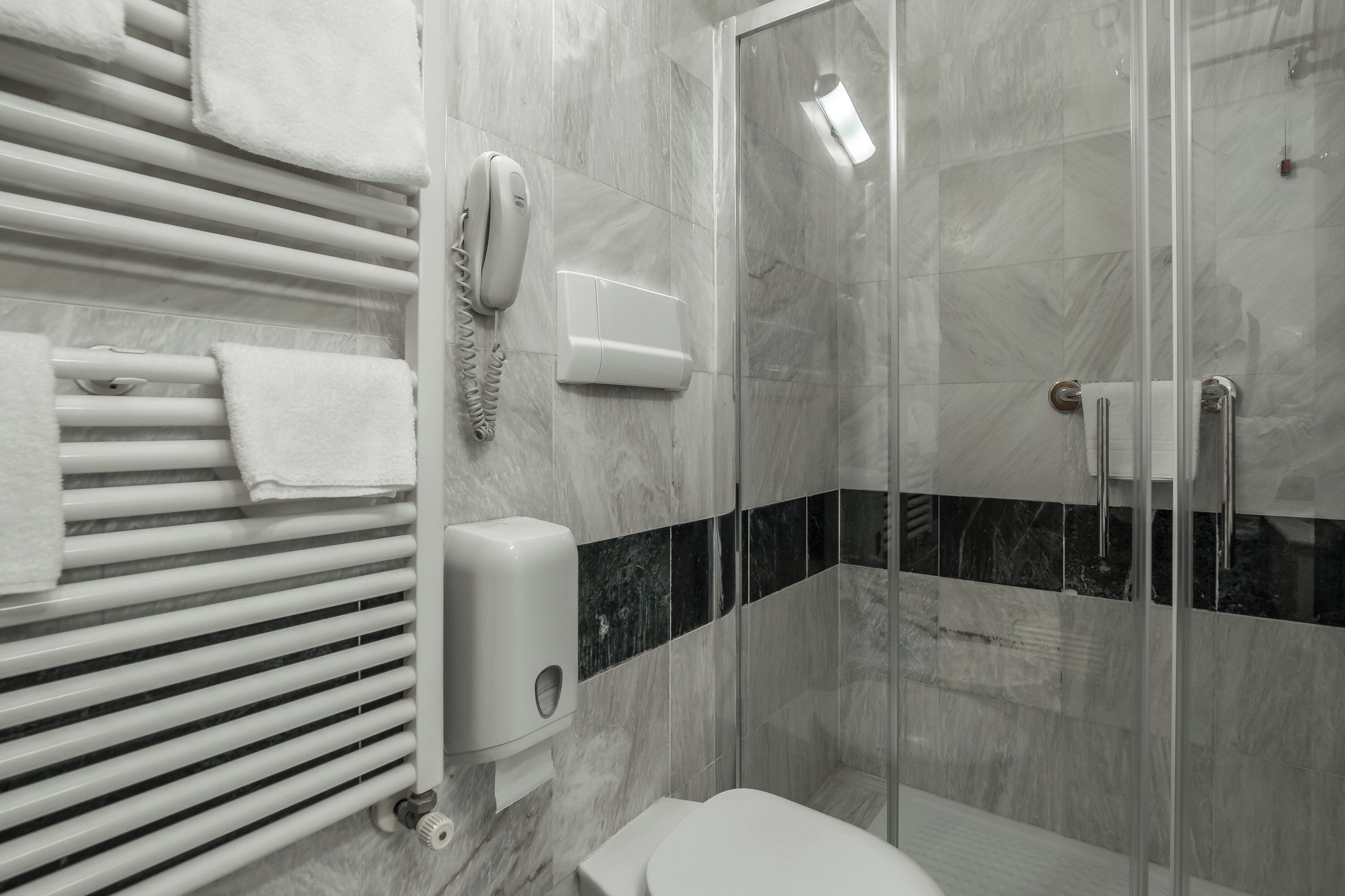 Un baño moderno con cabina de ducha de vidrio, inodoro, toallero y secador de manos.