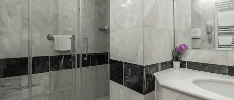 A modern bathroom with a glass shower enclosure, a marble-tiled shower area, a white sink, and a mirror with a towel rack.