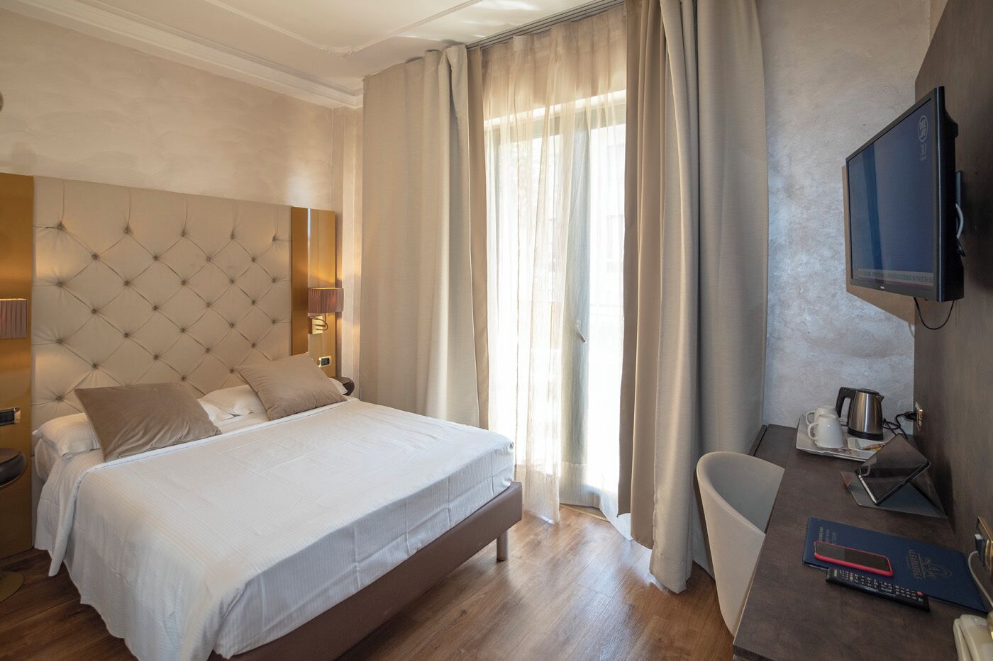 A hotel room with a large bed, a desk with a television, and a window with curtains.