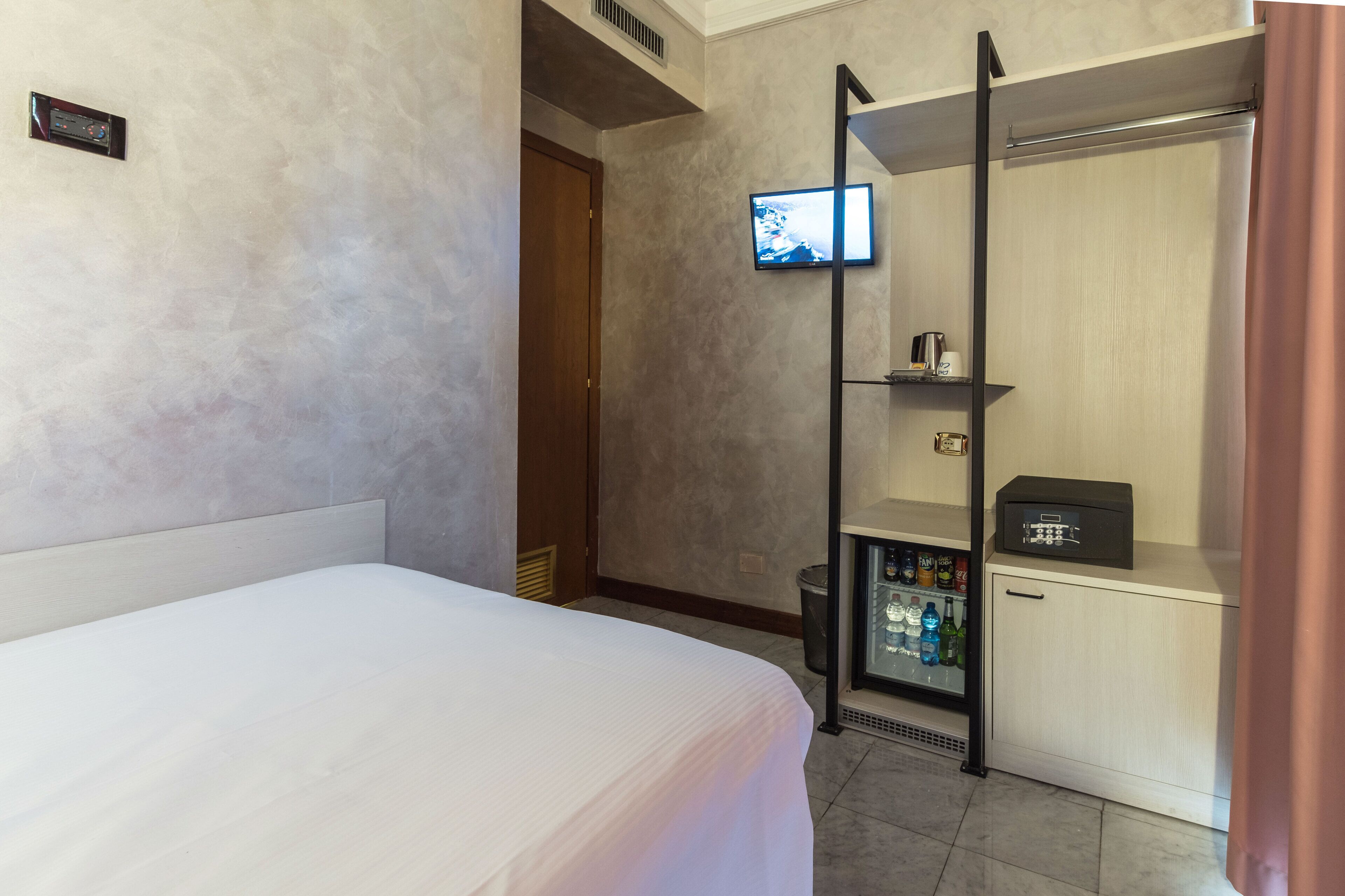 Habitación de hotel con cama, televisión montada en la pared, minibar y zona de ducha.