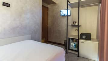 Ein Hotelzimmer mit Bett, einem an der Wand montierten Fernseher, einer Minibar und einer Duschkabine.