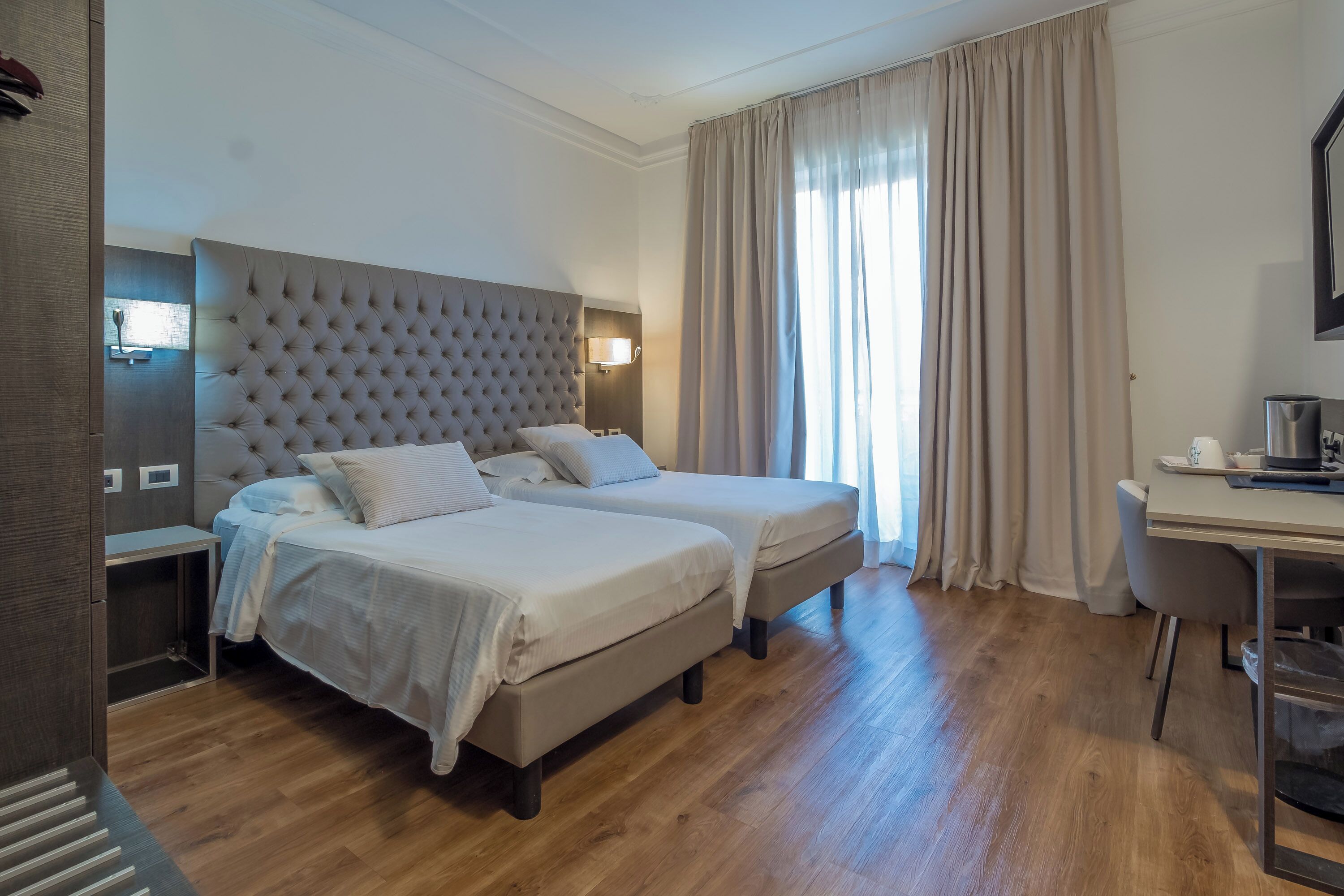 Ein Hotelzimmer mit zwei Betten, einem Schreibtisch und einem großen Fenster mit Vorhängen.