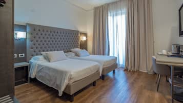 Ein Hotelzimmer mit zwei Betten, einem Schreibtisch und einem großen Fenster mit Vorhängen.