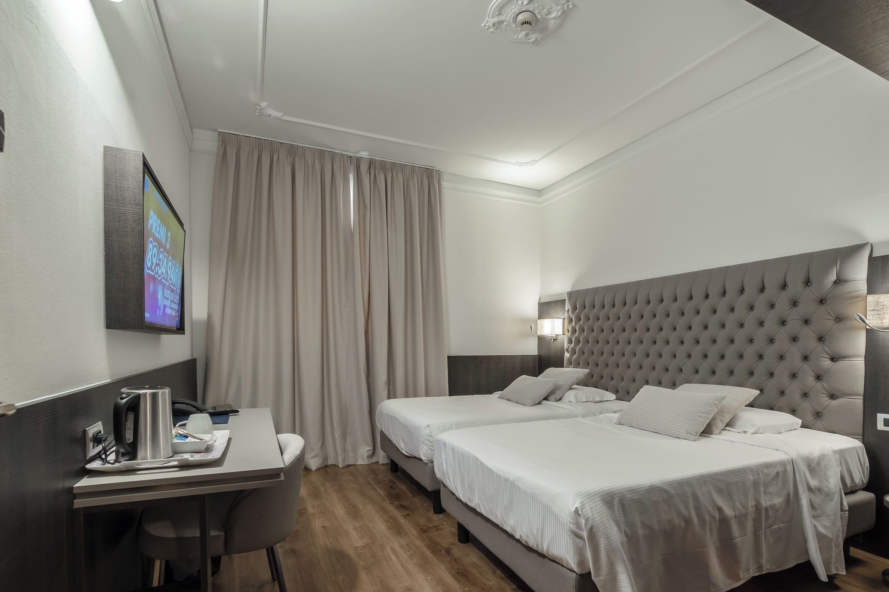 Une chambre d’hôtel avec un lit, des tables de chevet, un bureau avec une bouilloire et un téléviseur fixé au mur.