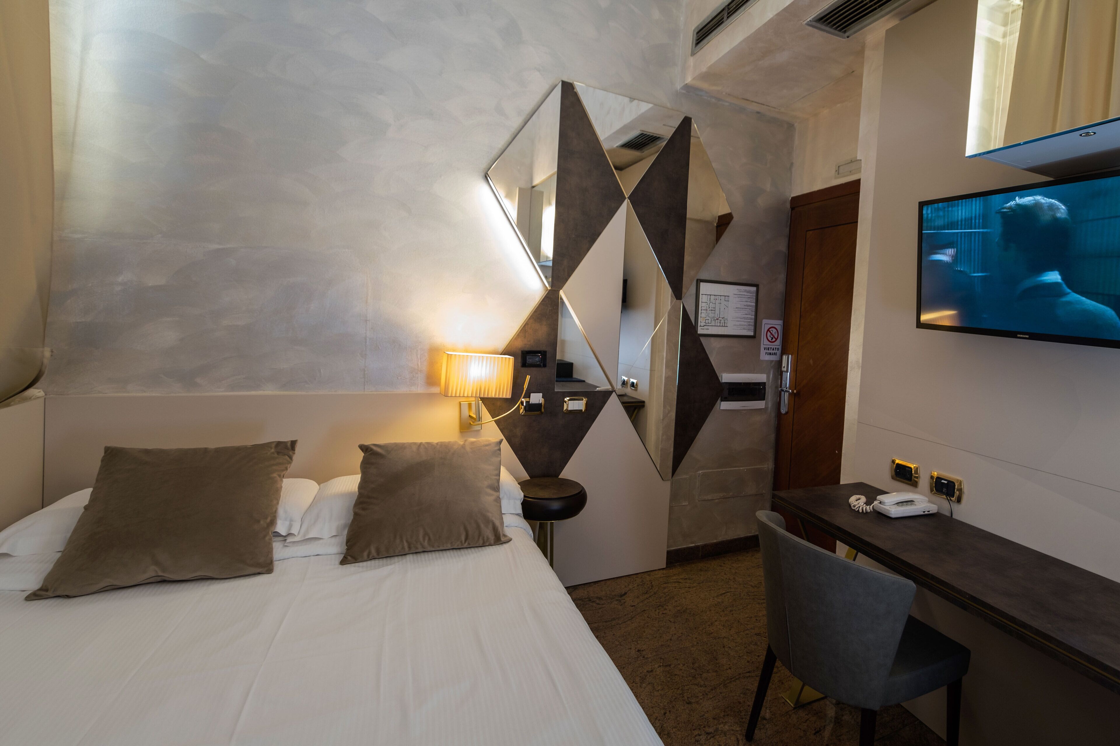 A hotel room with a bed, a desk, a chair, a TV, and a lamp.
