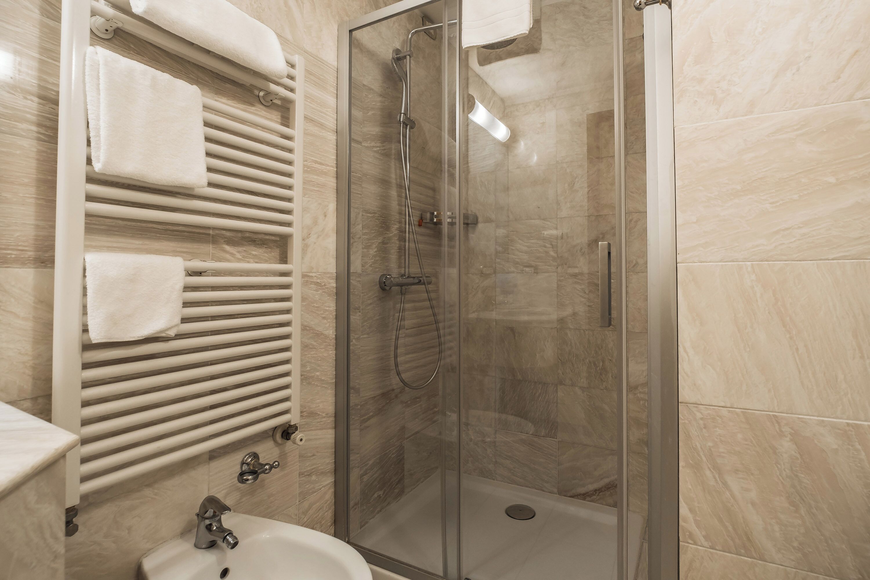 A bathroom with a glass-enclosed shower, a white sink, and a towel rack with multiple towels.