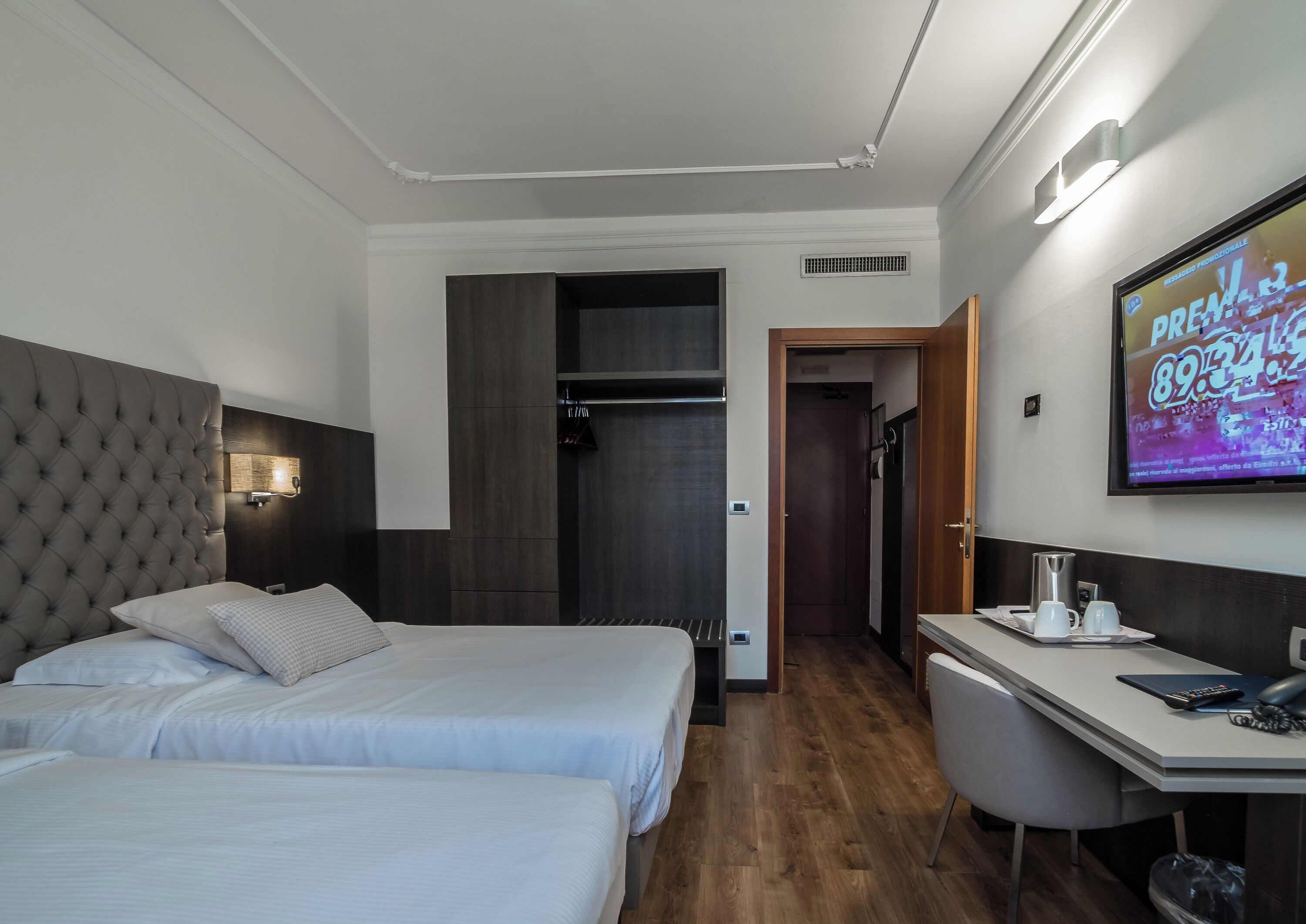 Quarto de hotel com duas camas, uma escrivaninha, uma televisão e um guarda-roupa.