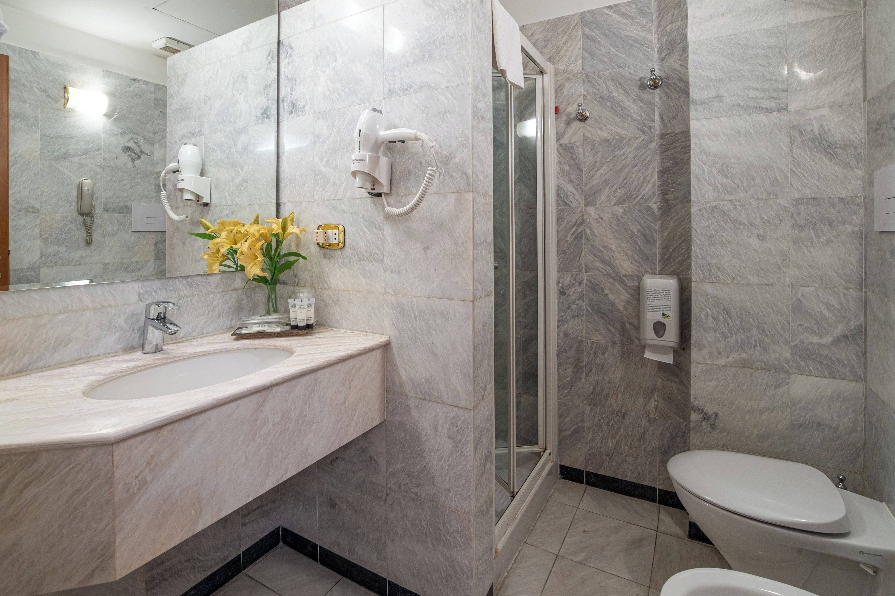 A modern bathroom with a marble sink, a glass shower enclosure, and a toilet.