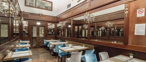Un restaurante con paneles de madera, sillas de terciopelo azul y candelabros.