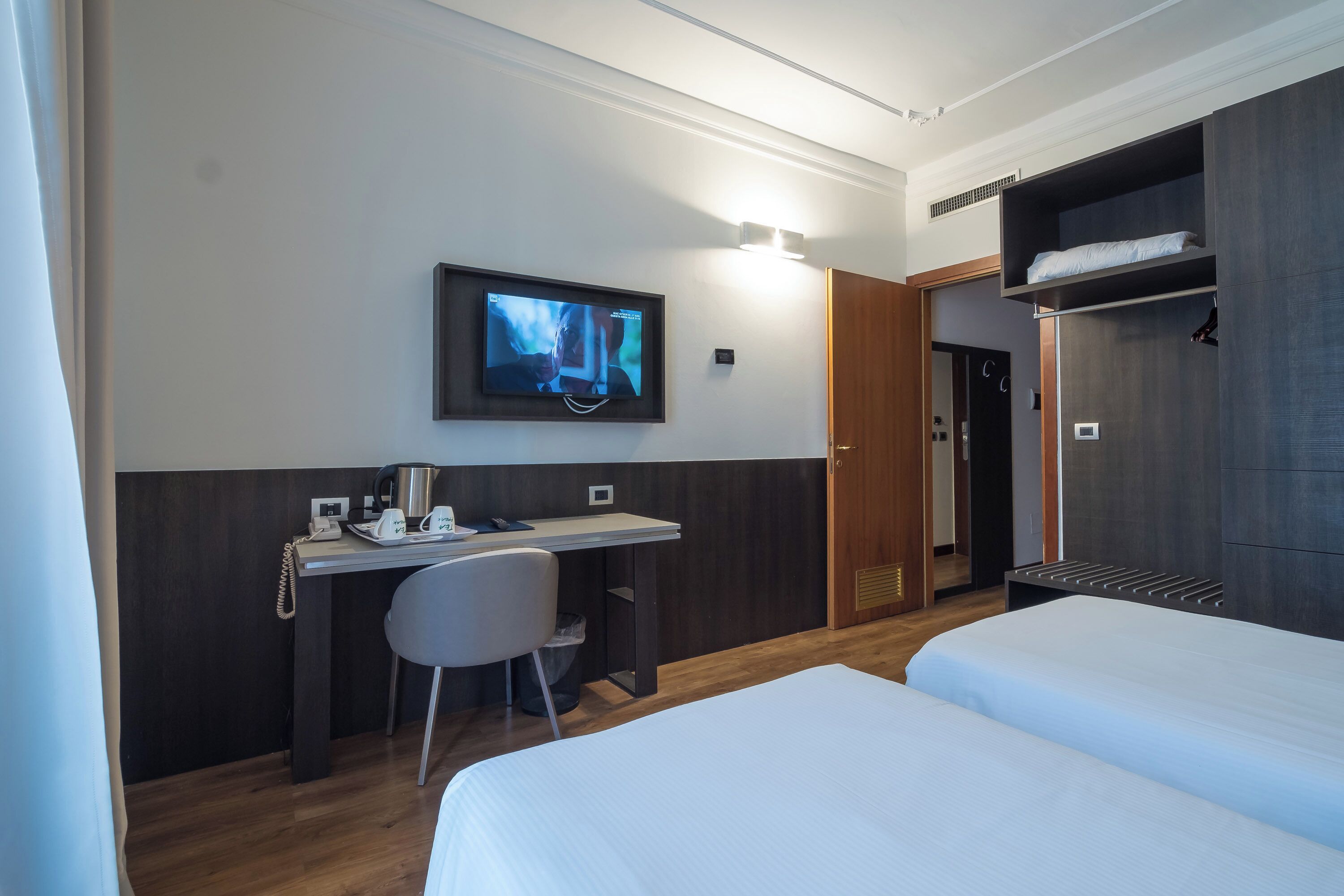 Una habitación de hotel con una cama, un escritorio con una silla, un televisor y un armario.