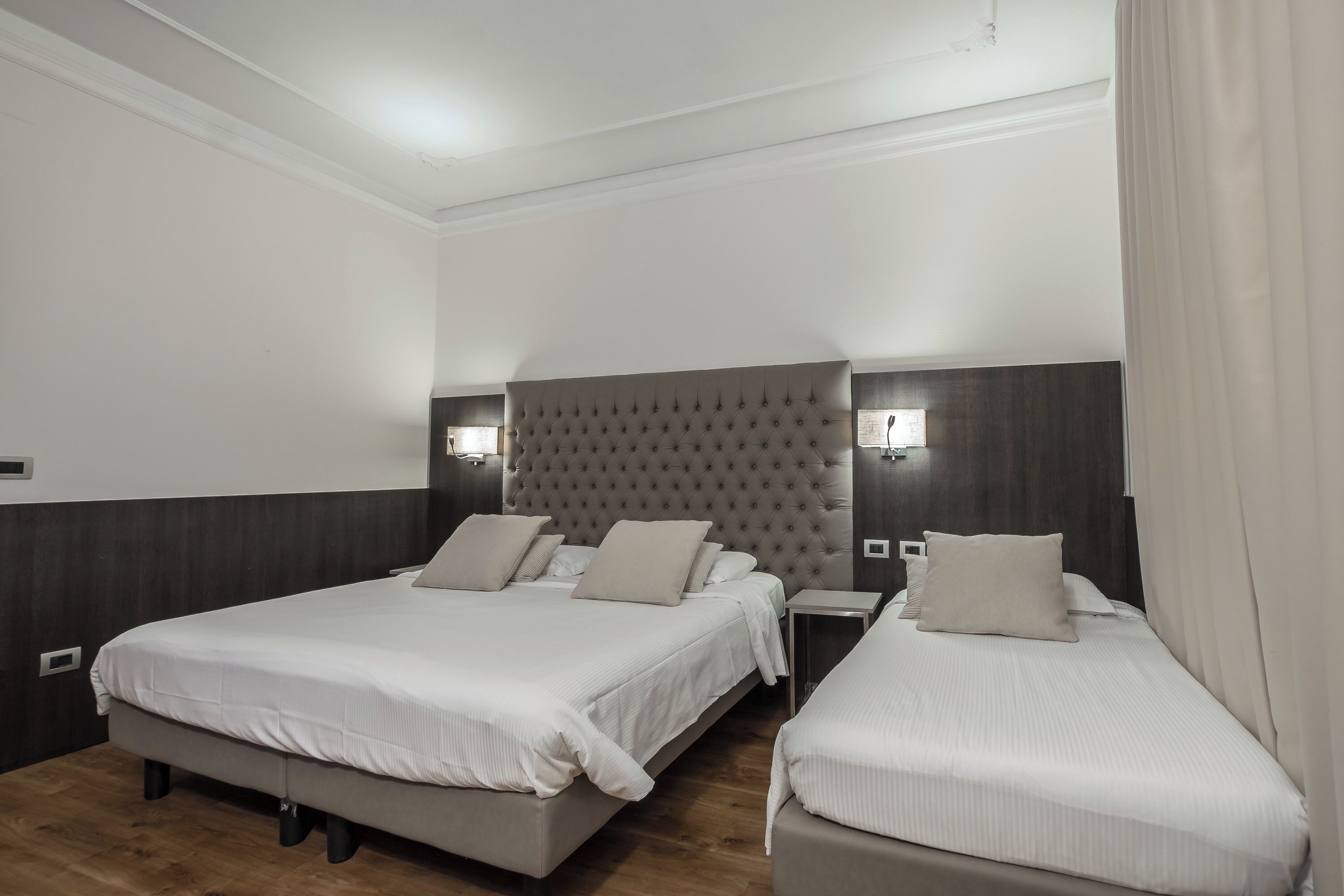Ein Hotelzimmer mit zwei Betten, einem gepolsterten Kopfteil, Nachttischen und einer neutralen Farbgestaltung.