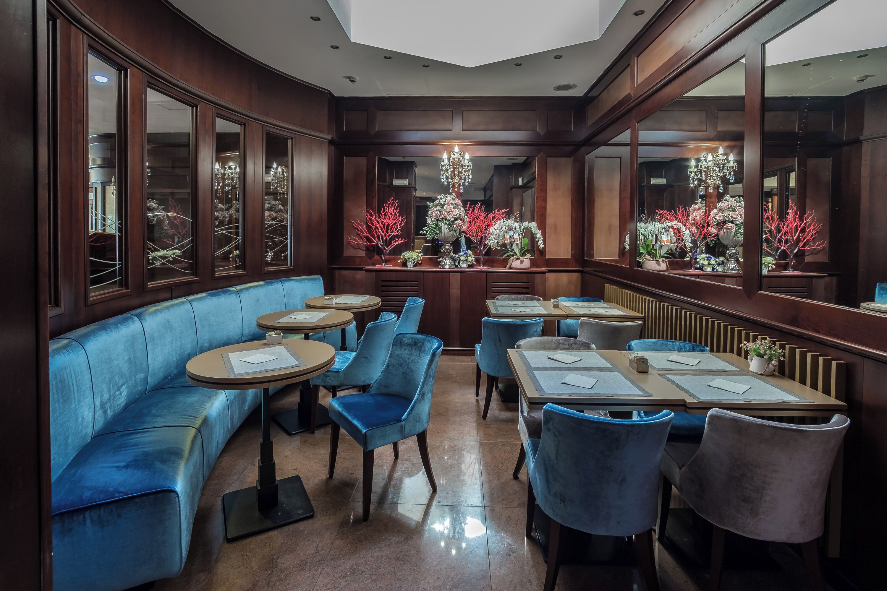 Un restaurante con asientos tapizados en azul, mesas redondas y un candelabro.