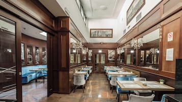 Un hall d’hôtel avec un long couloir, des boiseries, des lustres et des sièges recouverts d’un tissu bleu.