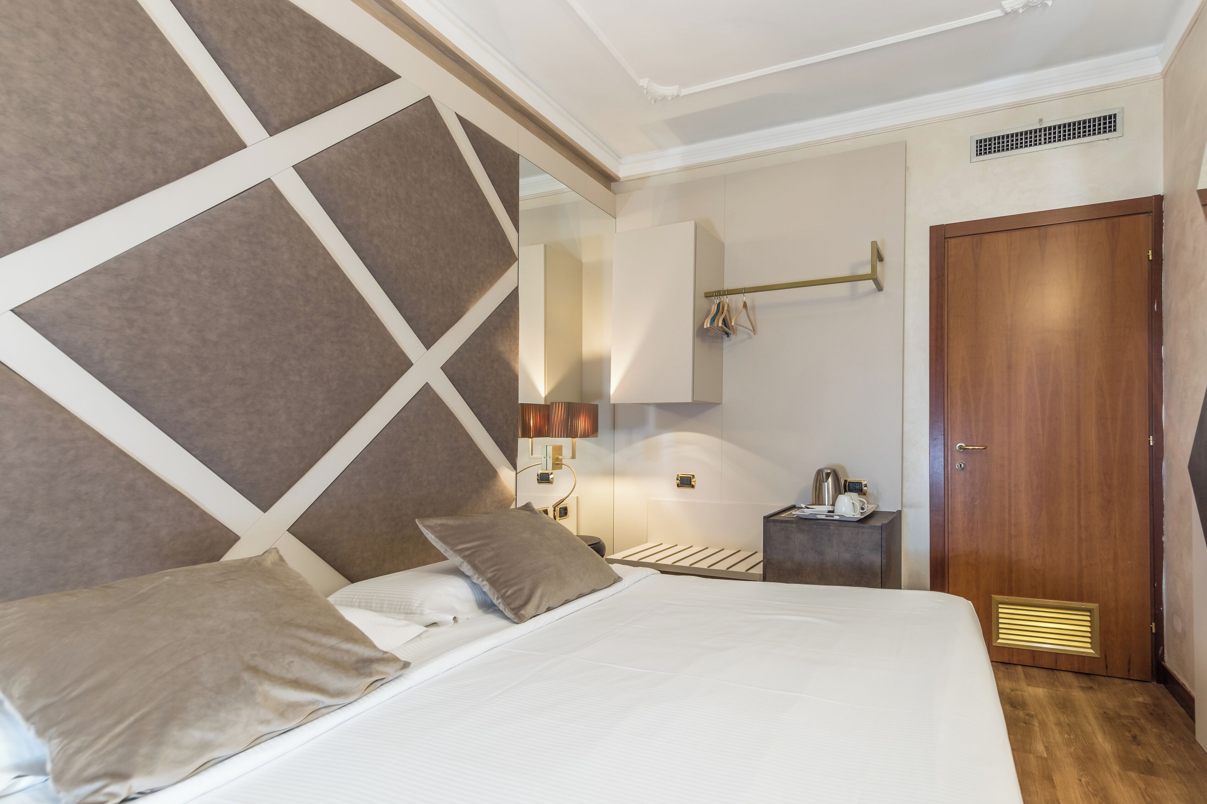 Ein Hotelzimmer mit einem großen Bett, einer Holztür, einem kleinen Nachttisch mit Lampe und einem Spiegel an der Wand.